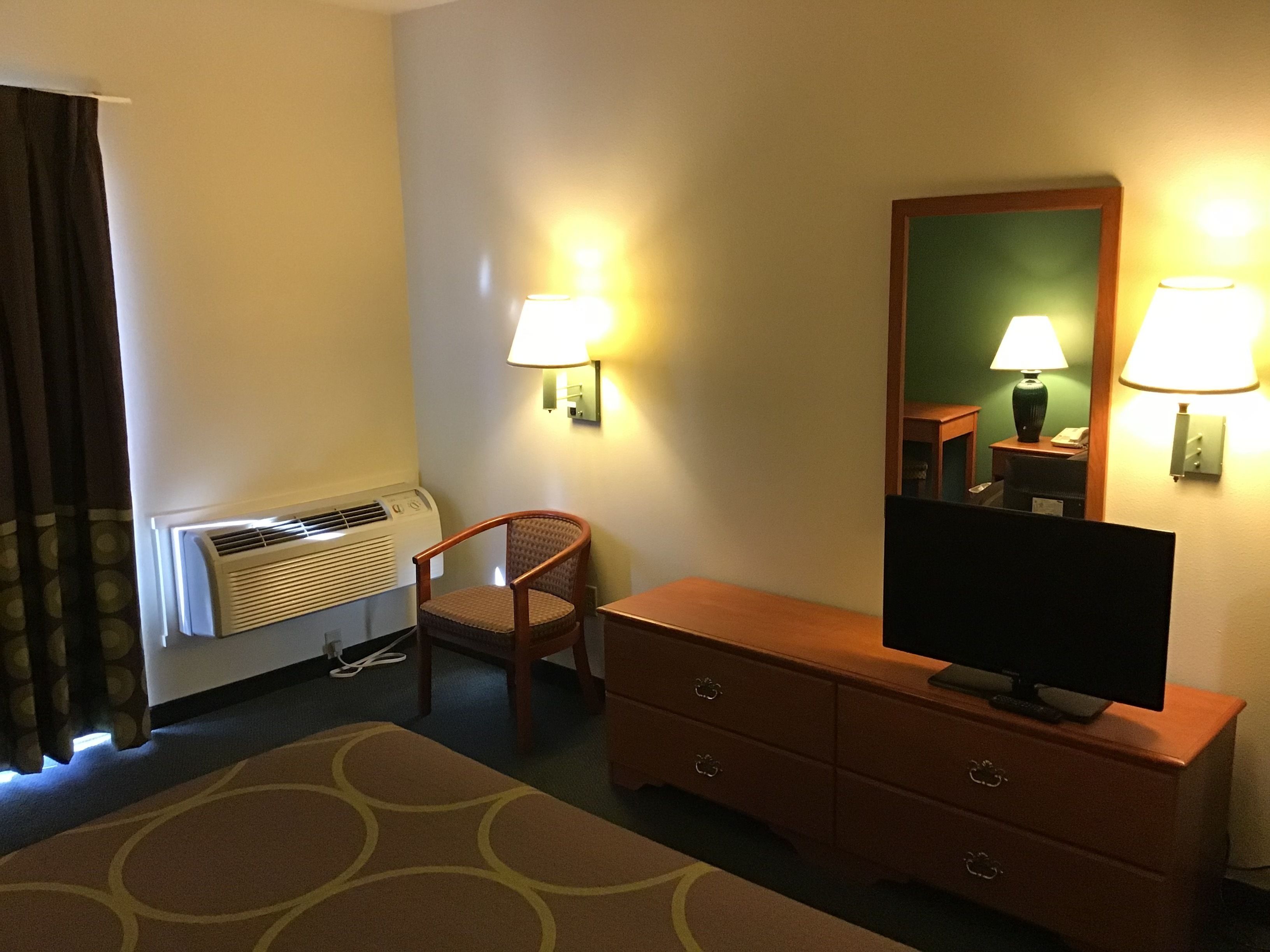 Habitación de hotel con cama, una silla, televisor sobre una cómoda de madera y lámparas fijadas en la pared.