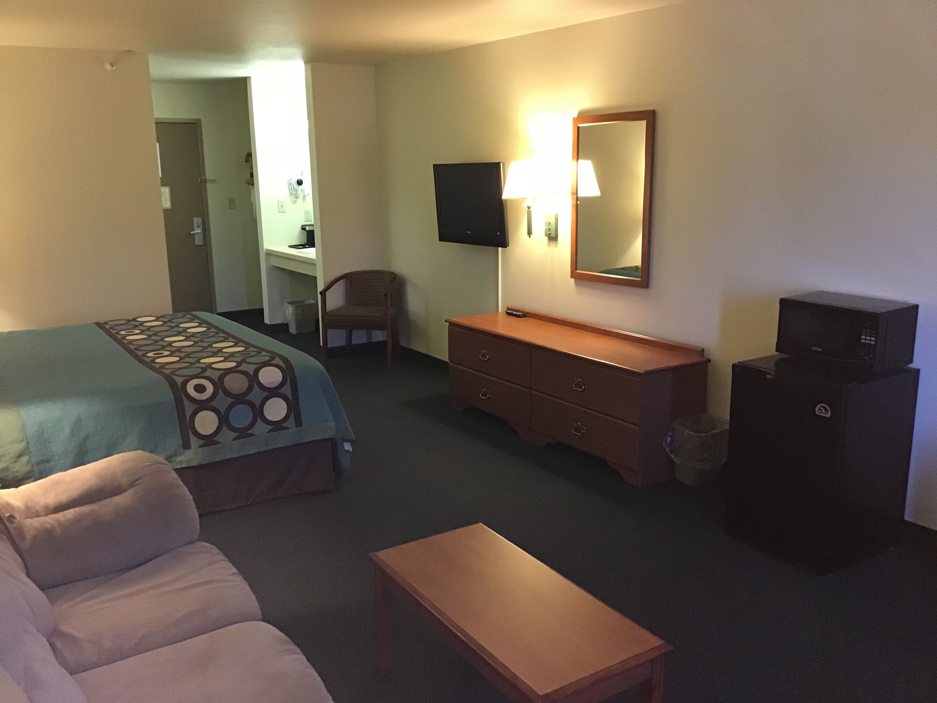 A hotel room with a bed, a desk, a chair, a dresser, a TV, and a microwave.