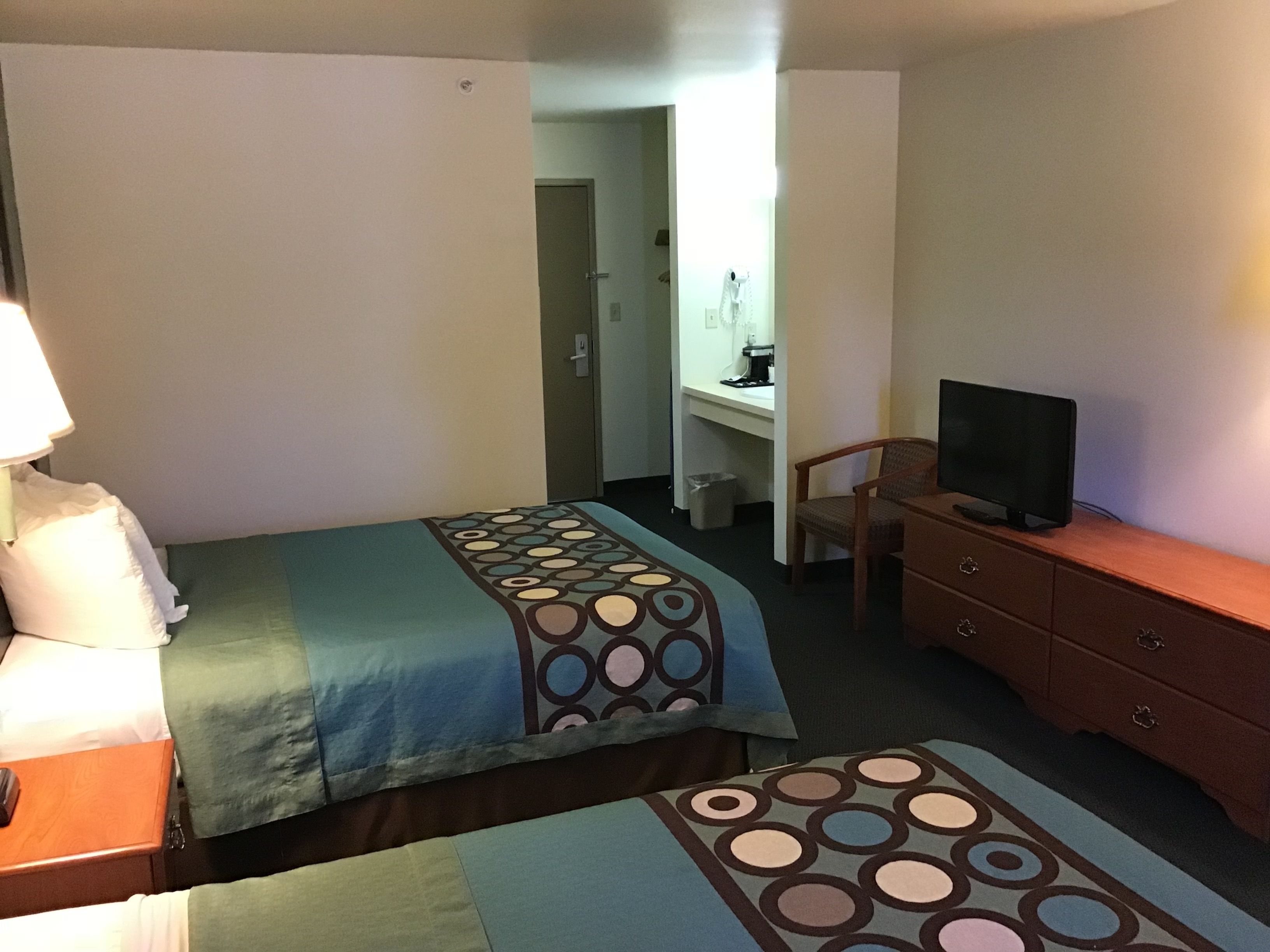 Ein Hotelzimmer mit zwei Betten, einem Schreibtisch mit Stuhl, einem Fernseher und einem Schminktisch.
