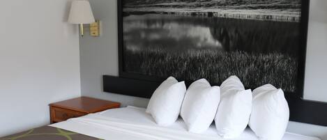 A hotel room with a large bed, a nightstand, a wall-mounted lamp, and a large framed picture of a landscape.