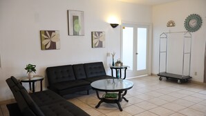A living room with a black sectional sofa, a glass coffee table, and two side tables. There are abstract floral paintings on the walls and a metal cart in the corner. - Super 8 by Wyndham Price (Price)