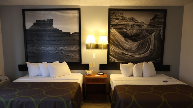 A hotel room with two beds, a nightstand with a lamp, and two framed pictures on the wall. - Super 8 by Wyndham Price (Price)