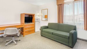 A hotel room with a desk, a green sofa, a television, a microwave, and a window with curtains. - Super 8 by Wyndham Price (Price)