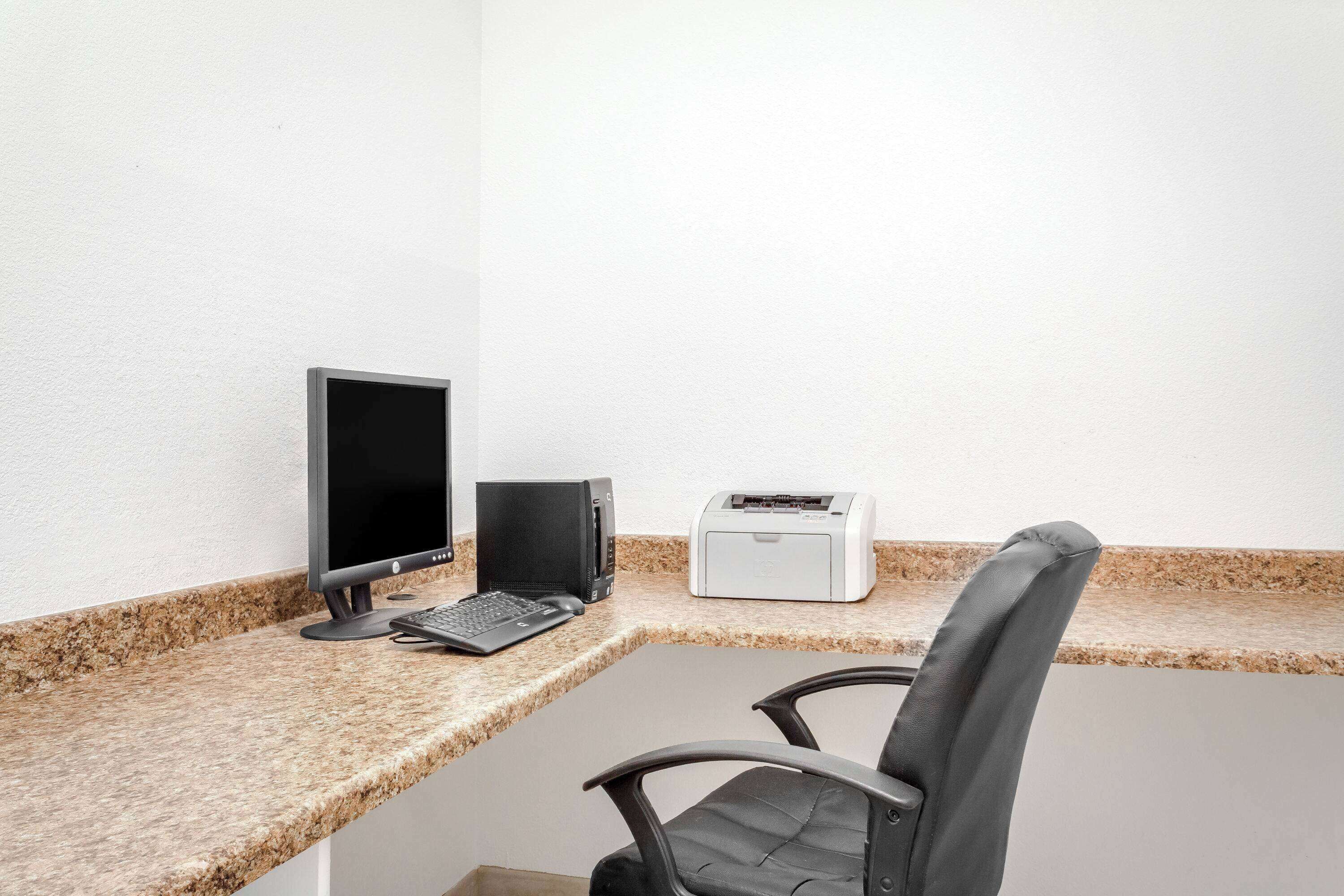 A workspace with a desktop computer, a laptop, a printer, and a chair.
