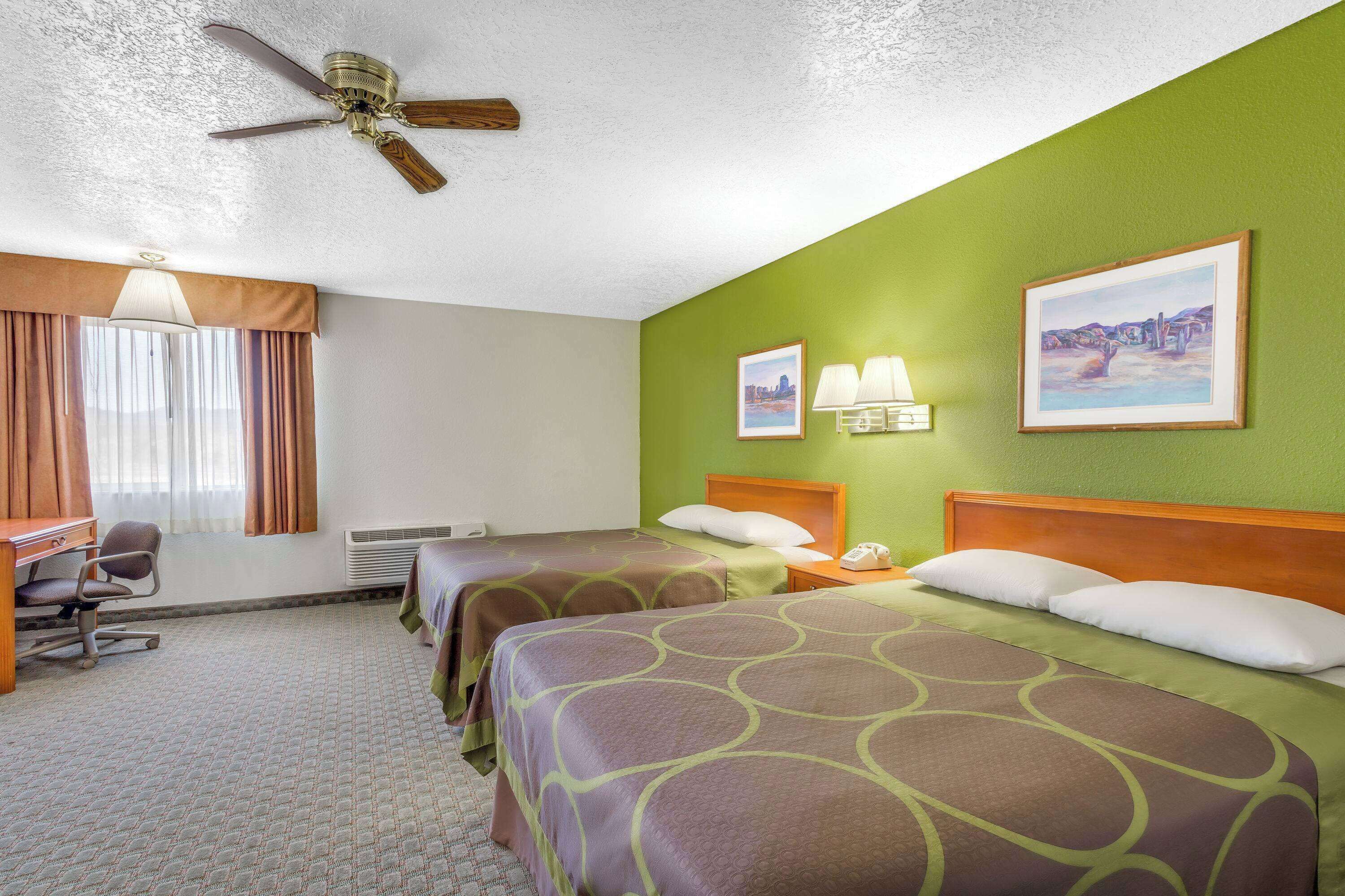 A hotel room with two beds, a desk, and a chair.