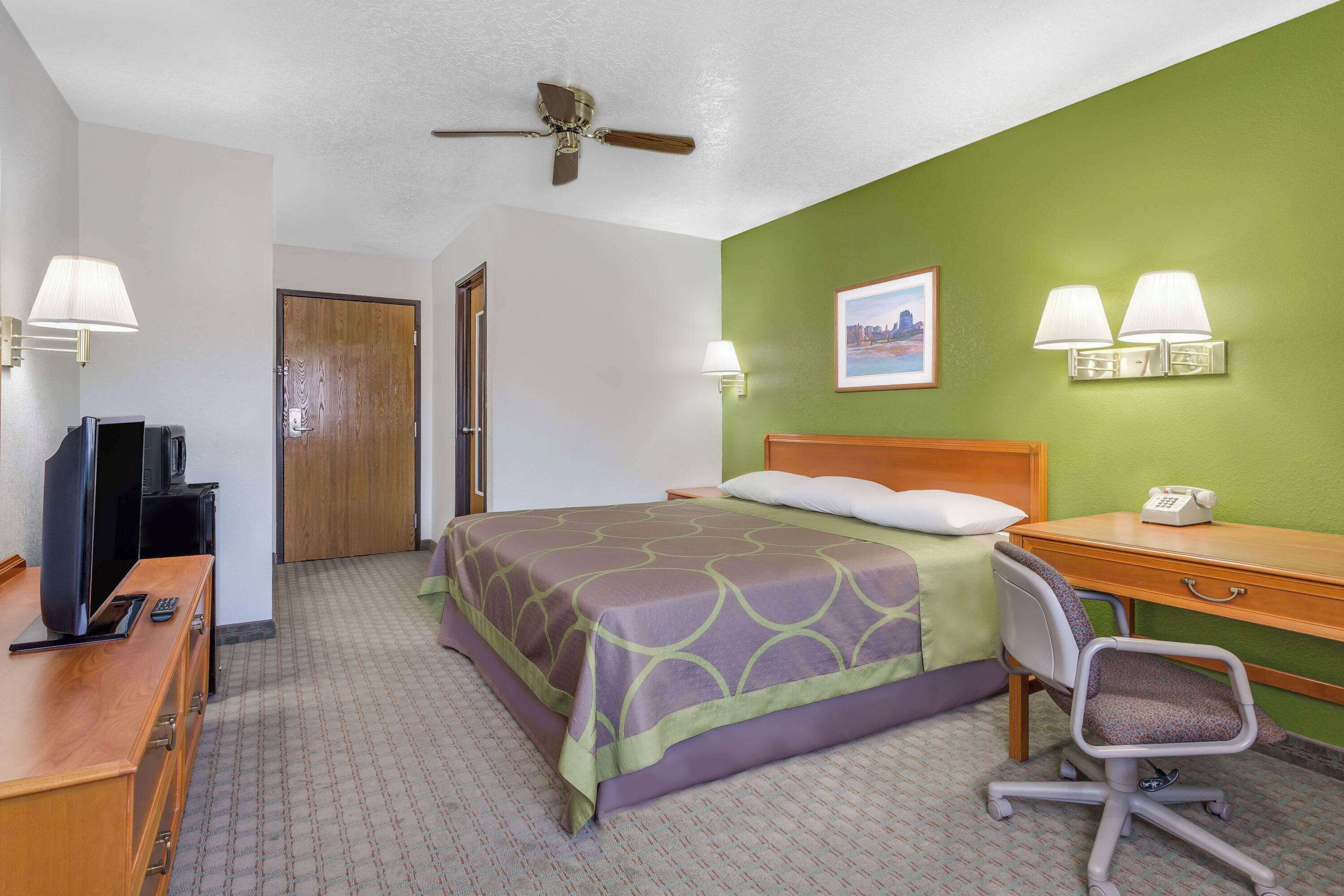 A hotel room with a bed, desk, chair, television, and a ceiling fan.