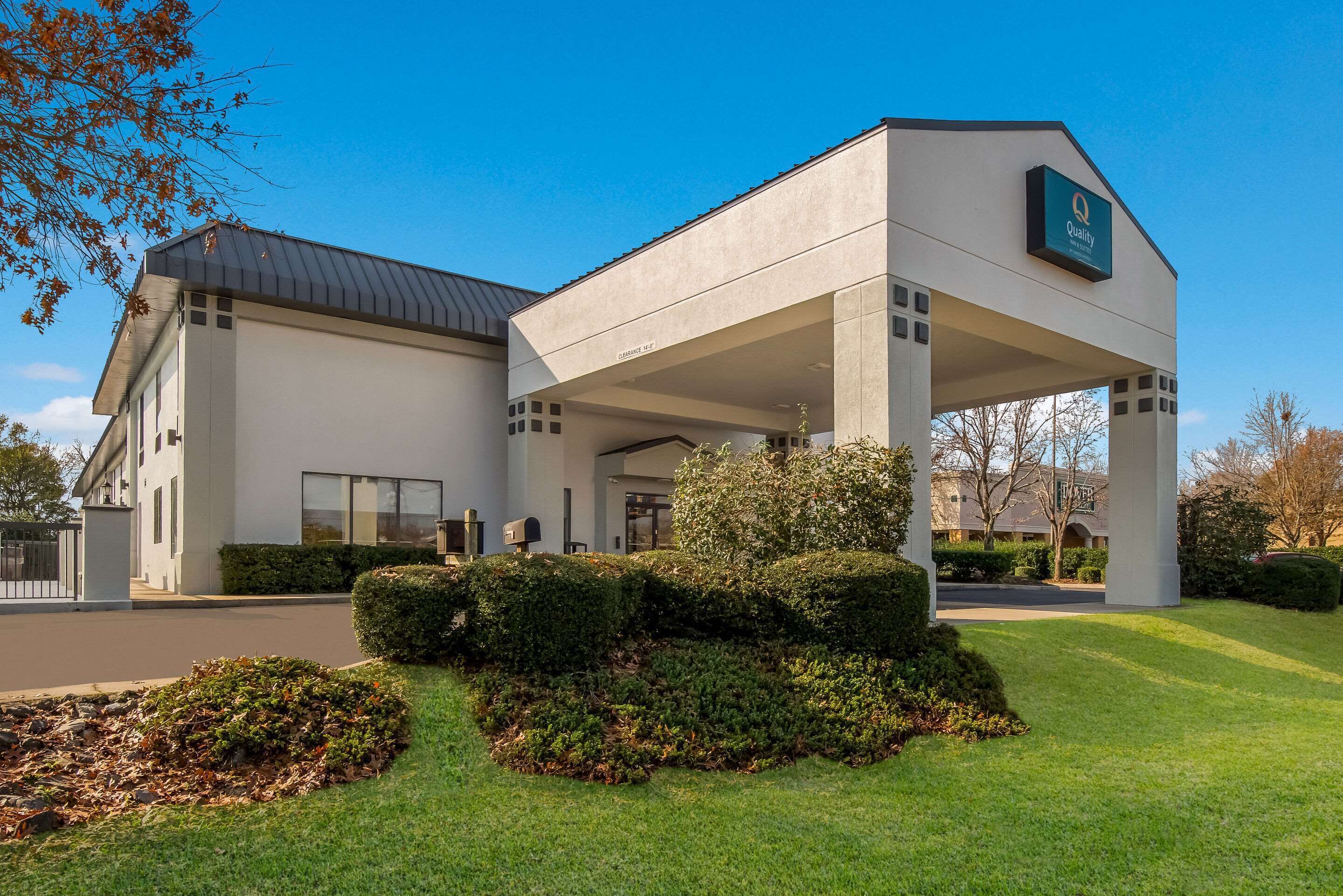 A modern hotel with a covered entrance, well-maintained lawns, and a clear blue sky.
