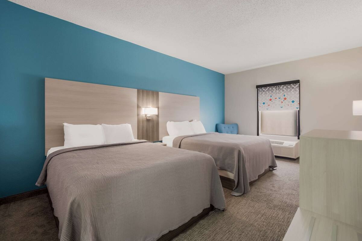 A hotel room with two beds, a large window with a view, and a wall-mounted air conditioning unit.