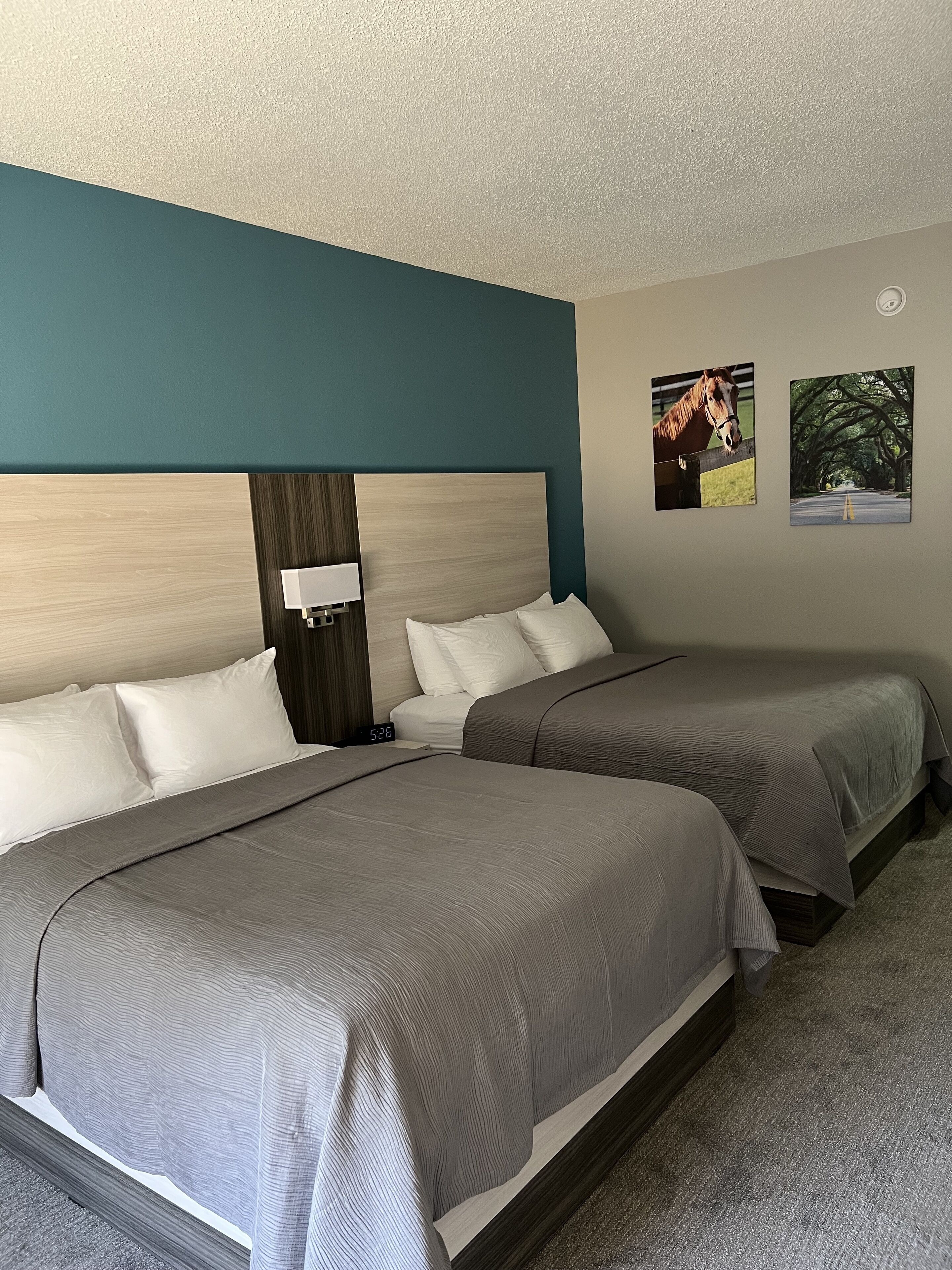 A hotel room with two beds, a nightstand, a clock, and two framed pictures on the wall.
