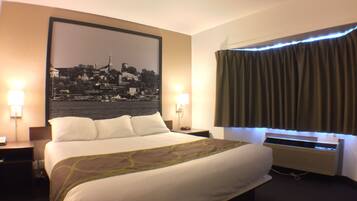 Une chambre d’hôtel avec un grand lit, deux lampes de chevet, un tableau représentant un paysage urbain accroché au mur, une fenêtre avec des rideaux et un appareil de climatisation.