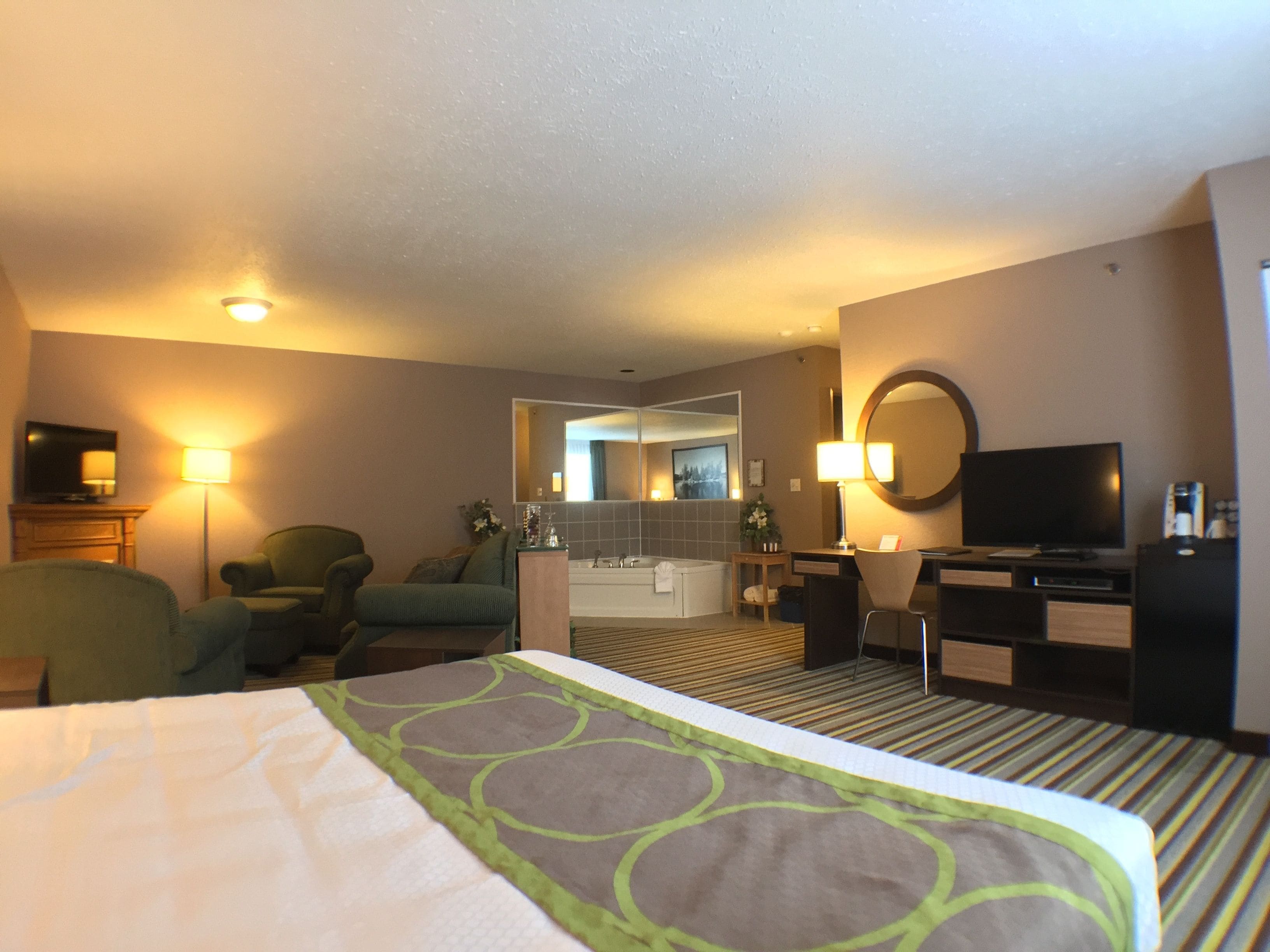 A hotel room with a bed, a desk, a chair, a television, a mirror, and a bathroom visible through an open door.