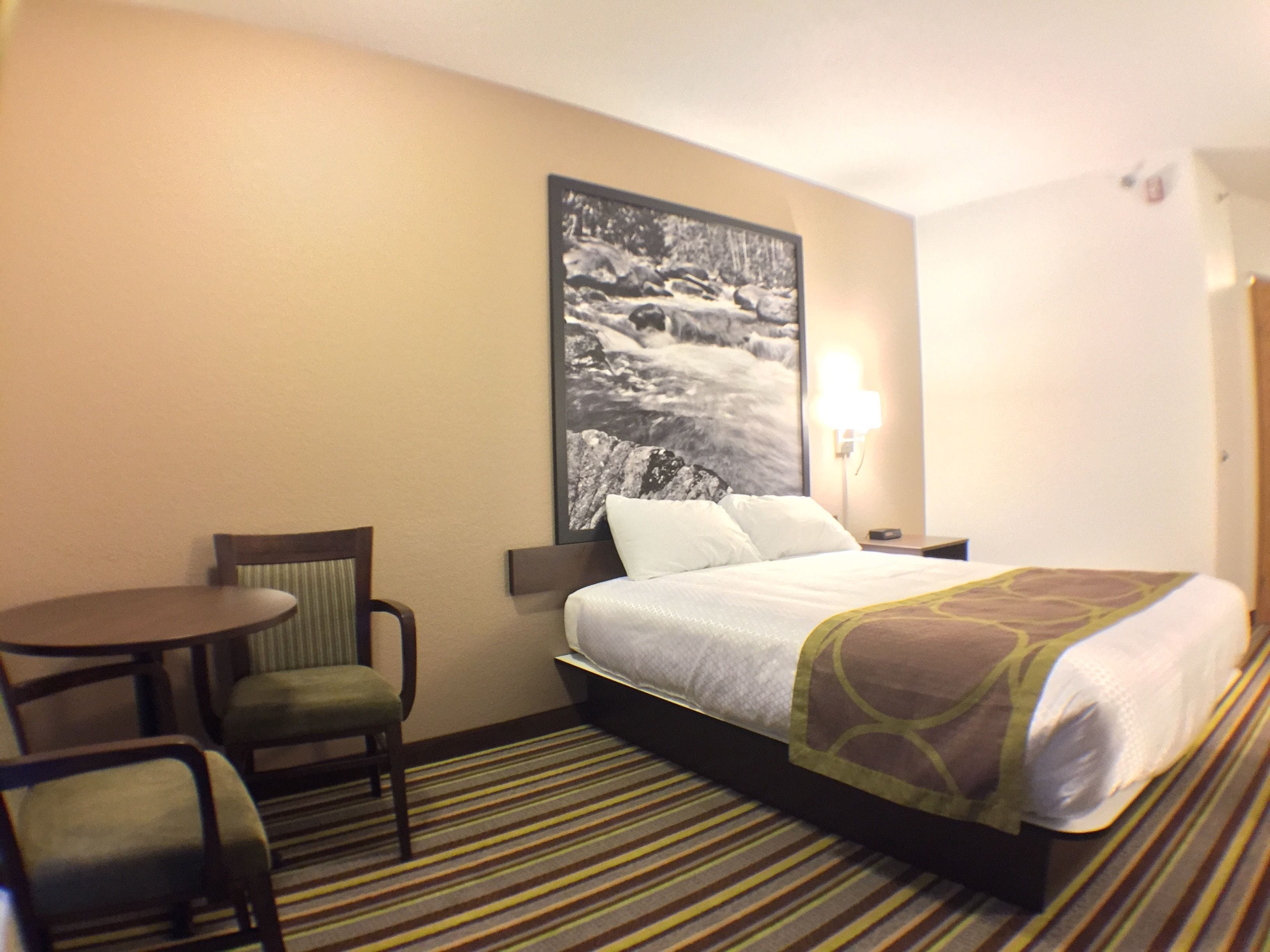 A hotel room with a bed, a chair, a small table, and a wall-mounted picture.