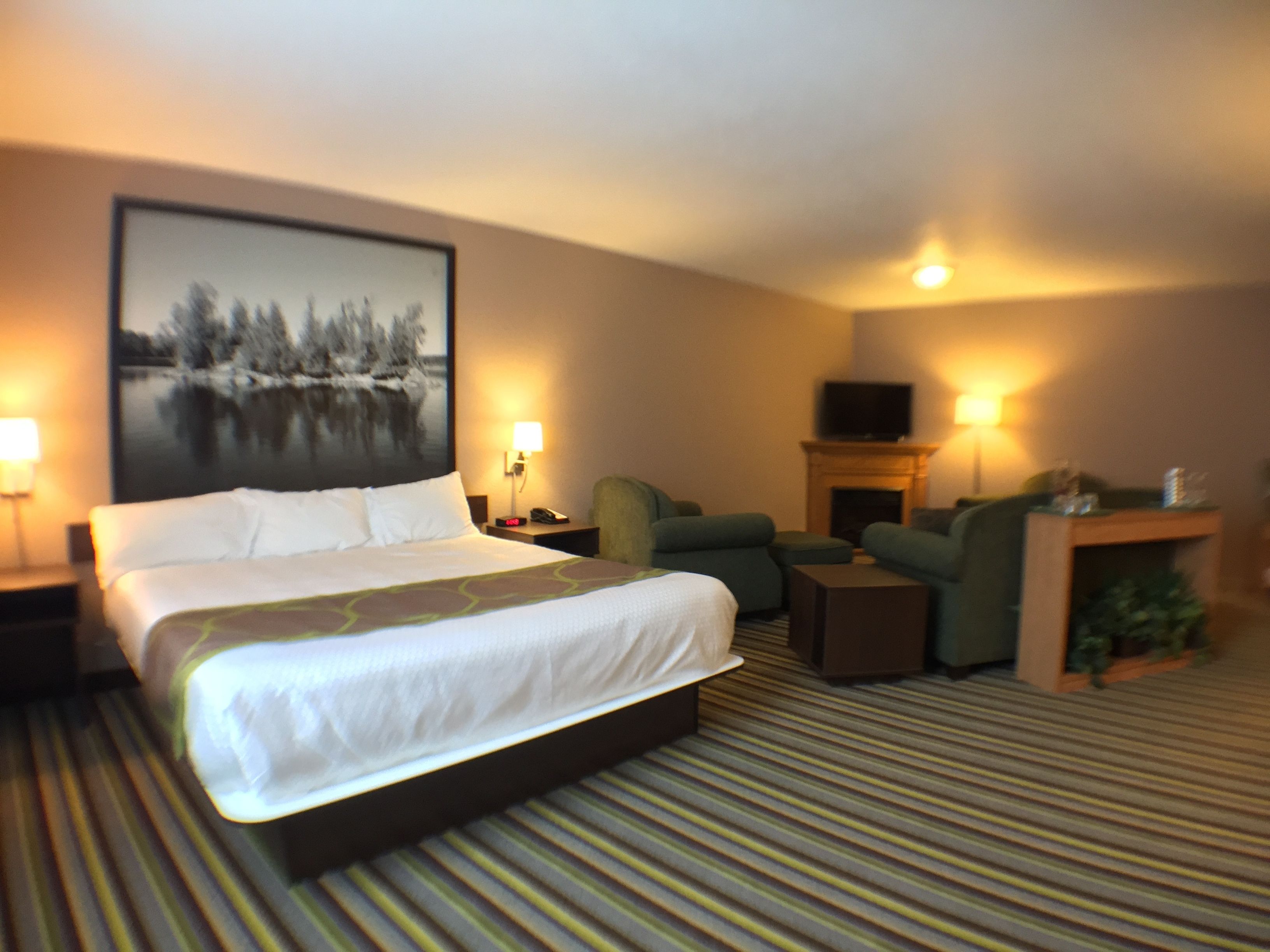A hotel room with a large bed, a sofa, a television, and a fireplace.