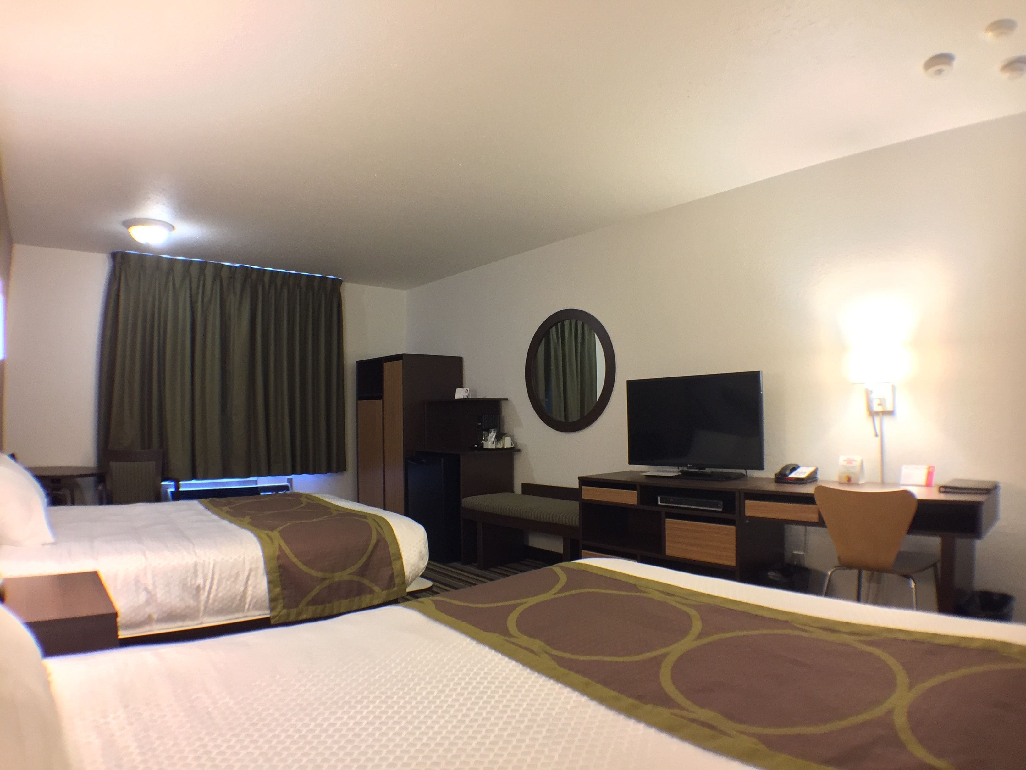 Habitación de hotel con dos camas, un escritorio, un televisor, un espejo y una lámpara.