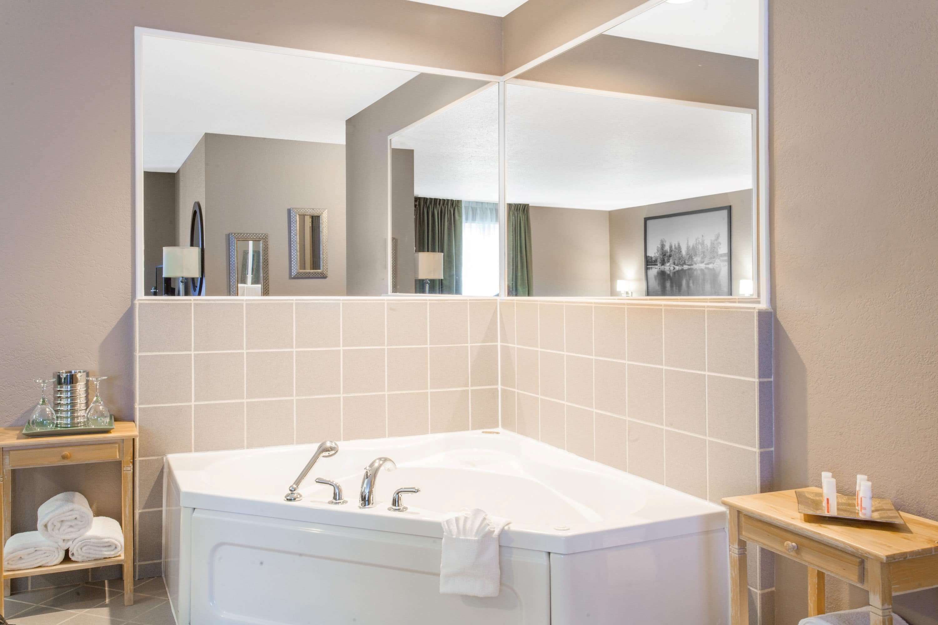 A modern bathroom with a large bathtub, a mirror, and a small table with towels and toiletries.