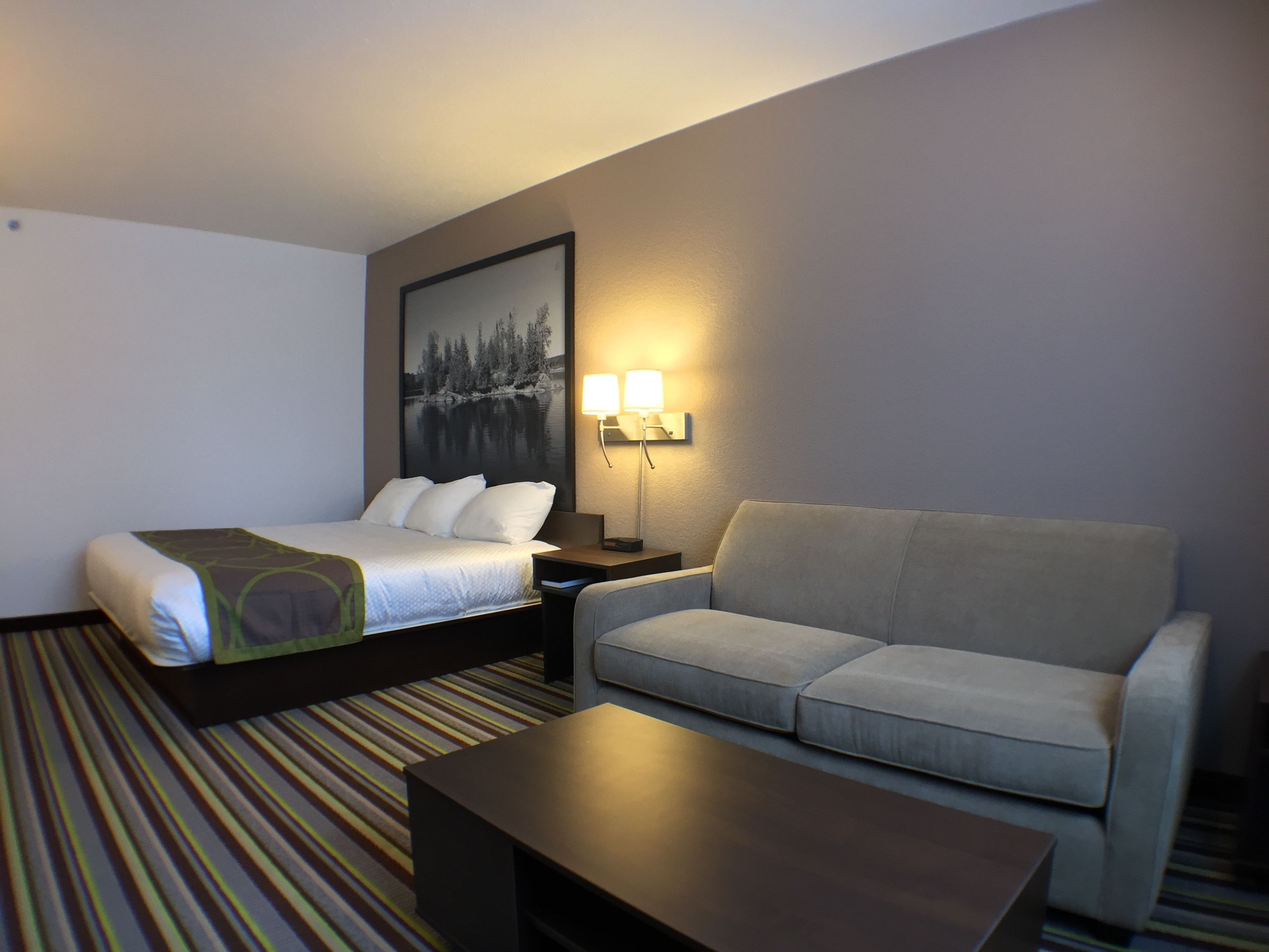 A hotel room with a bed, a sofa, a nightstand, a lamp, and a coffee table.