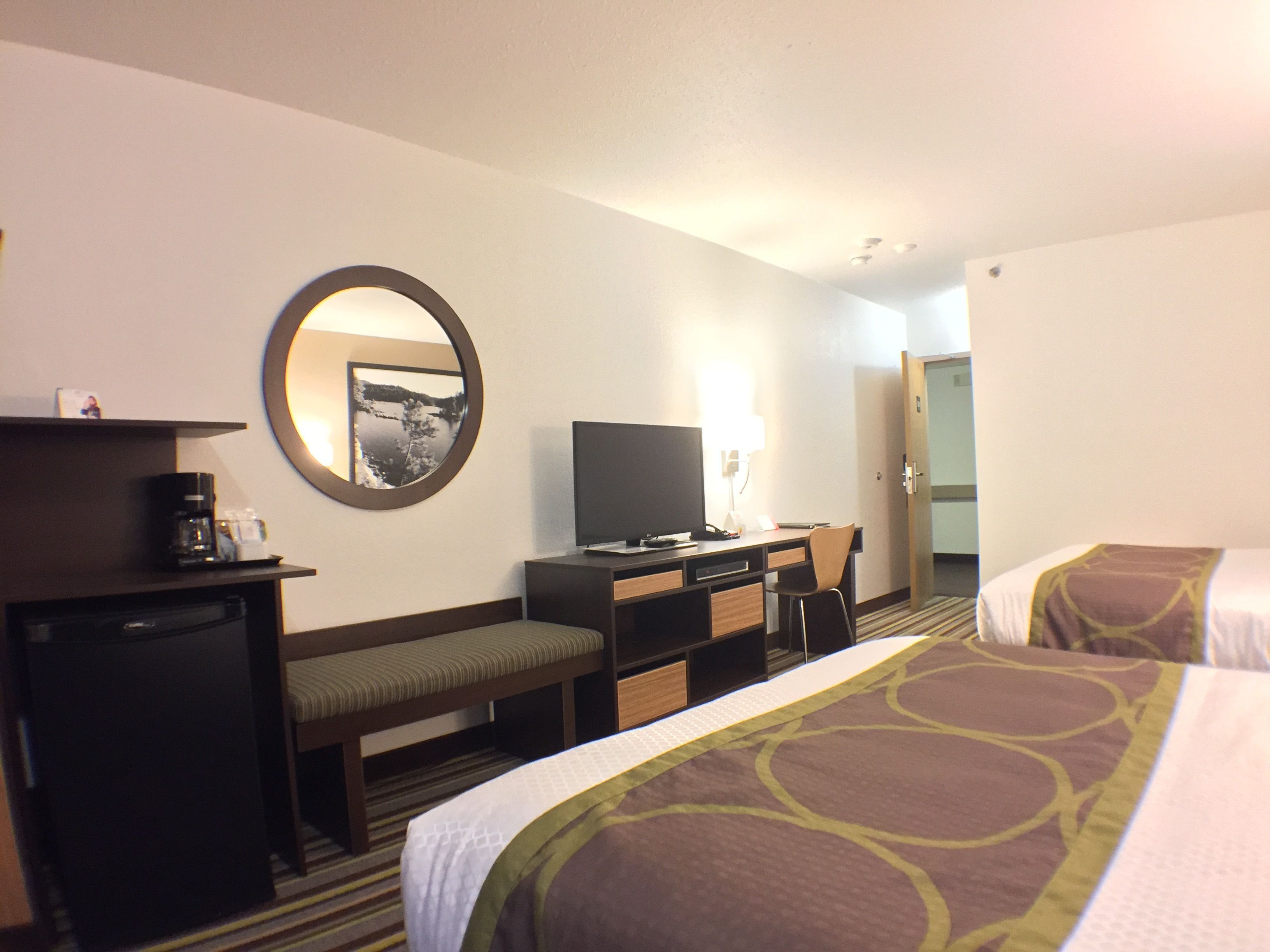 Een hotelkamer met een bed, een bureau, een televisie, een koffiezetapparaat en een spiegel.
