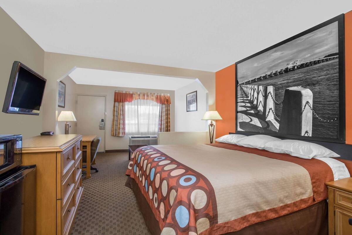 A hotel room with a bed, a desk, a television, a microwave, and a large painting on the wall.