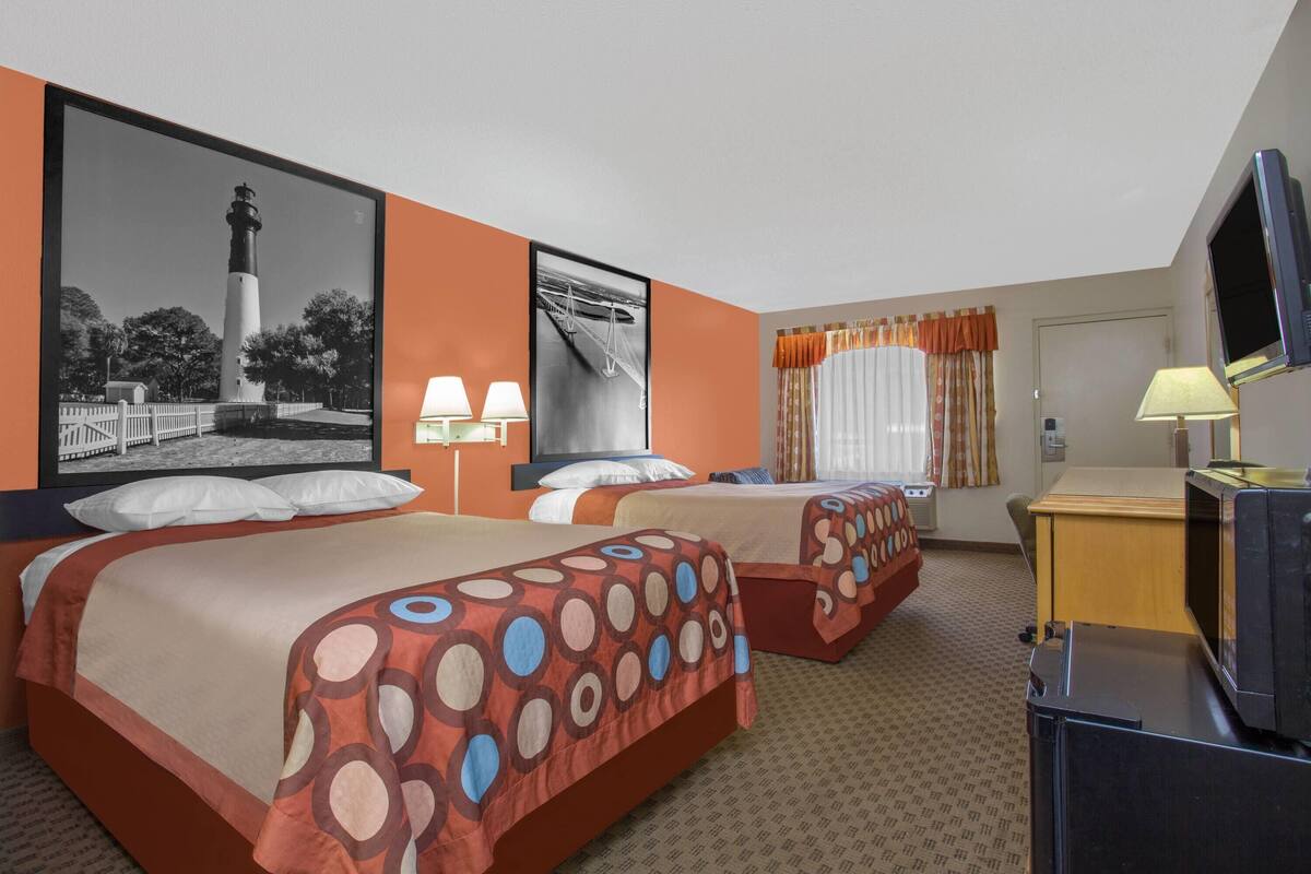 A hotel room with two beds, a television, and artwork on the walls.