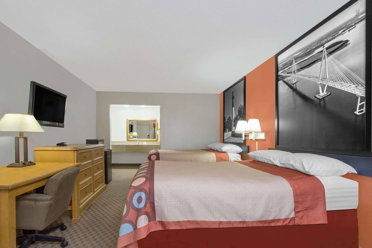 A hotel room with a bed, desk, chair, dresser, and a large framed picture on the wall.