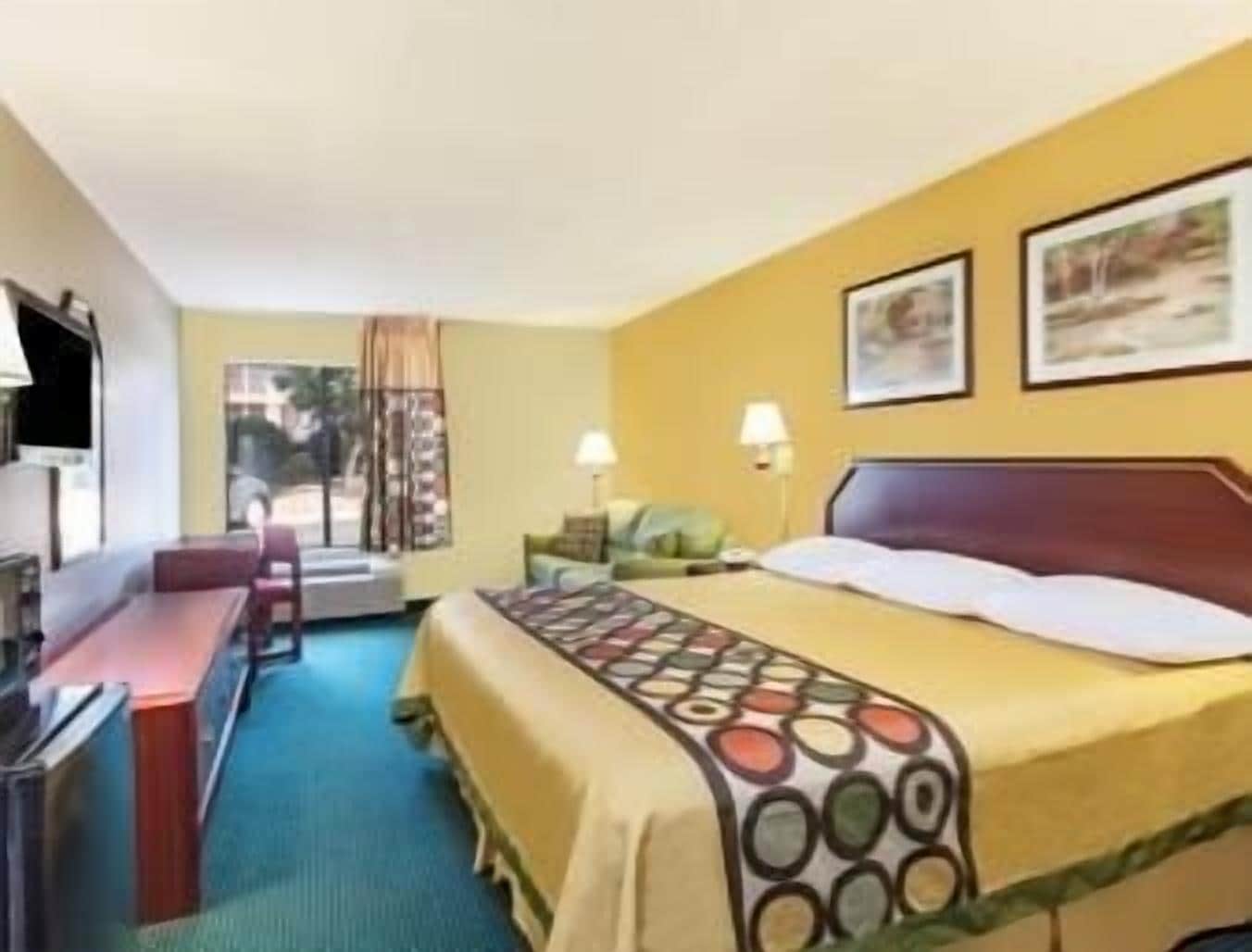 A hotel room with a bed, a desk, a chair, a TV, and a window with curtains.