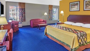 Habitación de hotel con una cama grande, un sofá rojo, una mesita y un escritorio con lámpara.