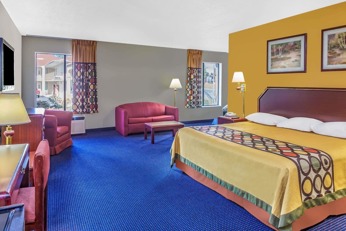 Habitación de hotel con una cama grande, un sofá rojo, una mesita y un escritorio con lámpara.