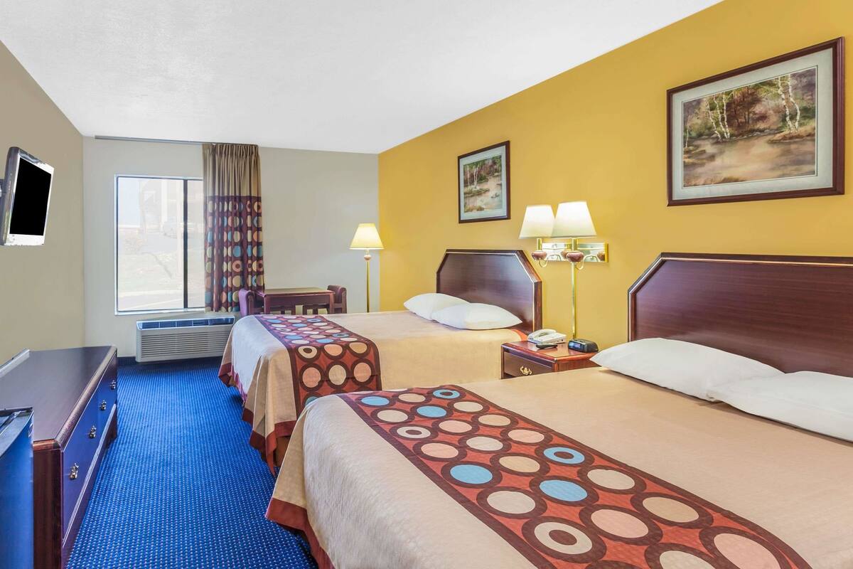 Habitación de hotel con dos camas, un escritorio, una silla, un televisor y una ventana con cortinas.
