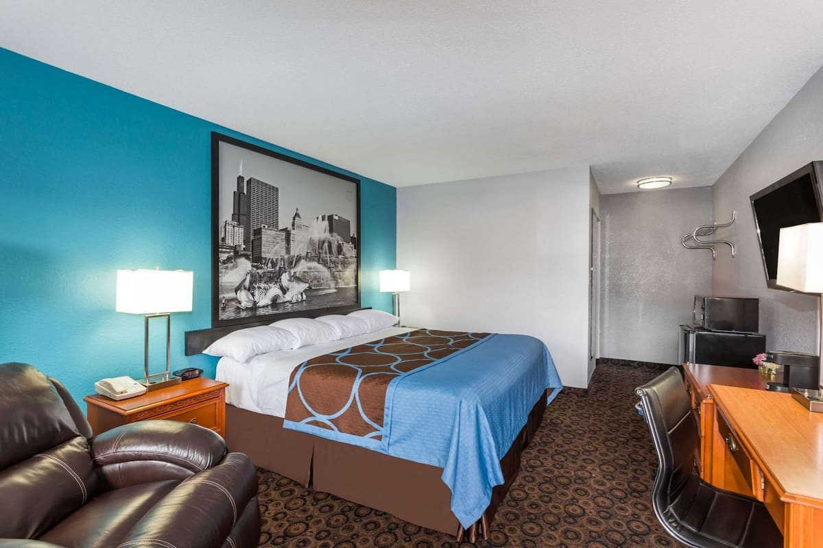 A hotel room with a bed, a desk, a chair, a telephone, and a television.