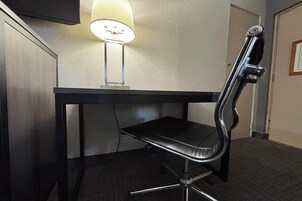 A desk with a chair, a lamp, and a door in a hotel room.