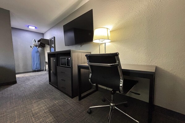 A hotel room with a desk, chair, television, lamp, and a microwave.