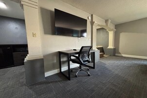 A room with a flat-screen TV mounted on the wall, a desk with a chair, and a carpeted floor.