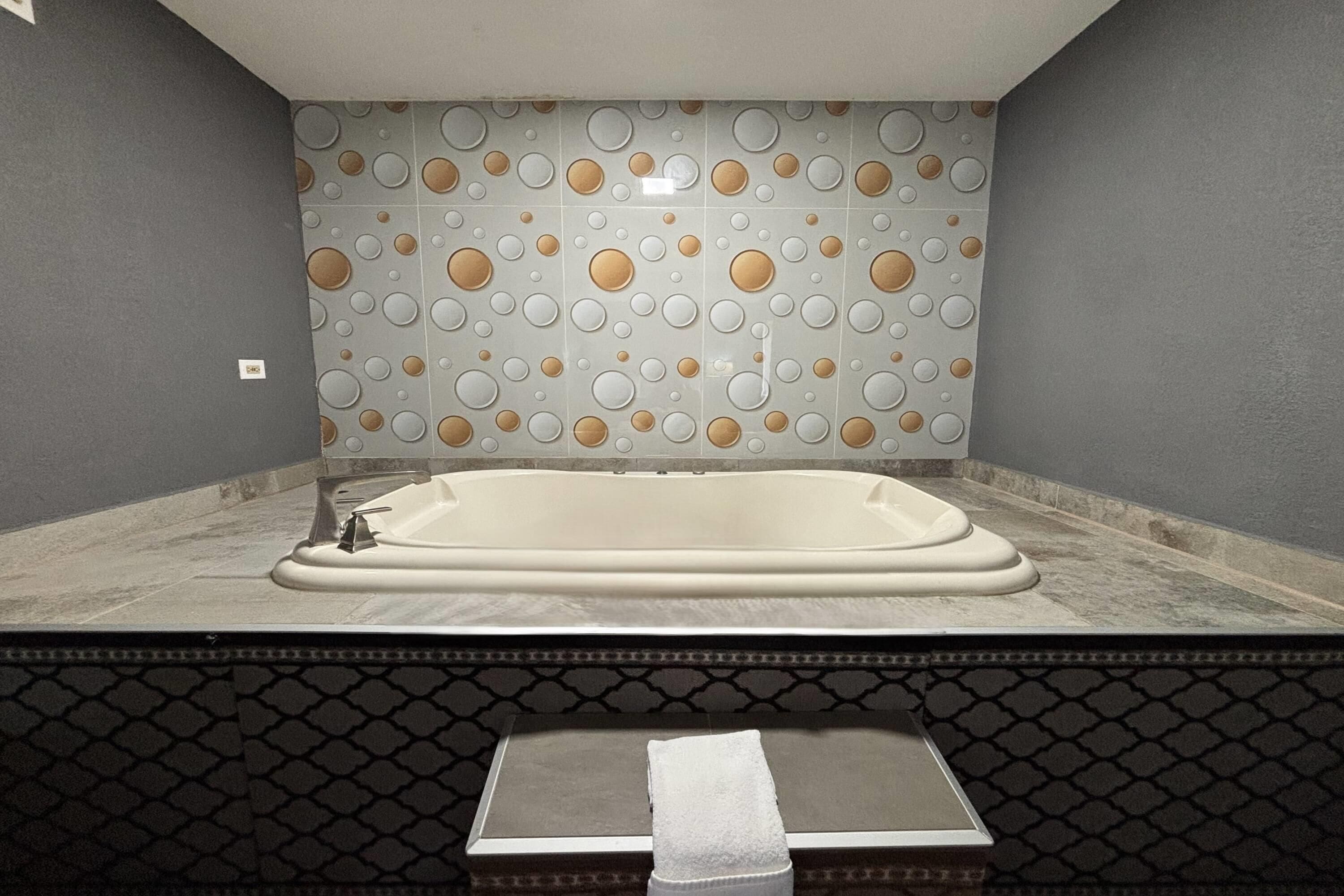 A modern bathroom with a freestanding bathtub, patterned wall tiles, and a textured floor.
