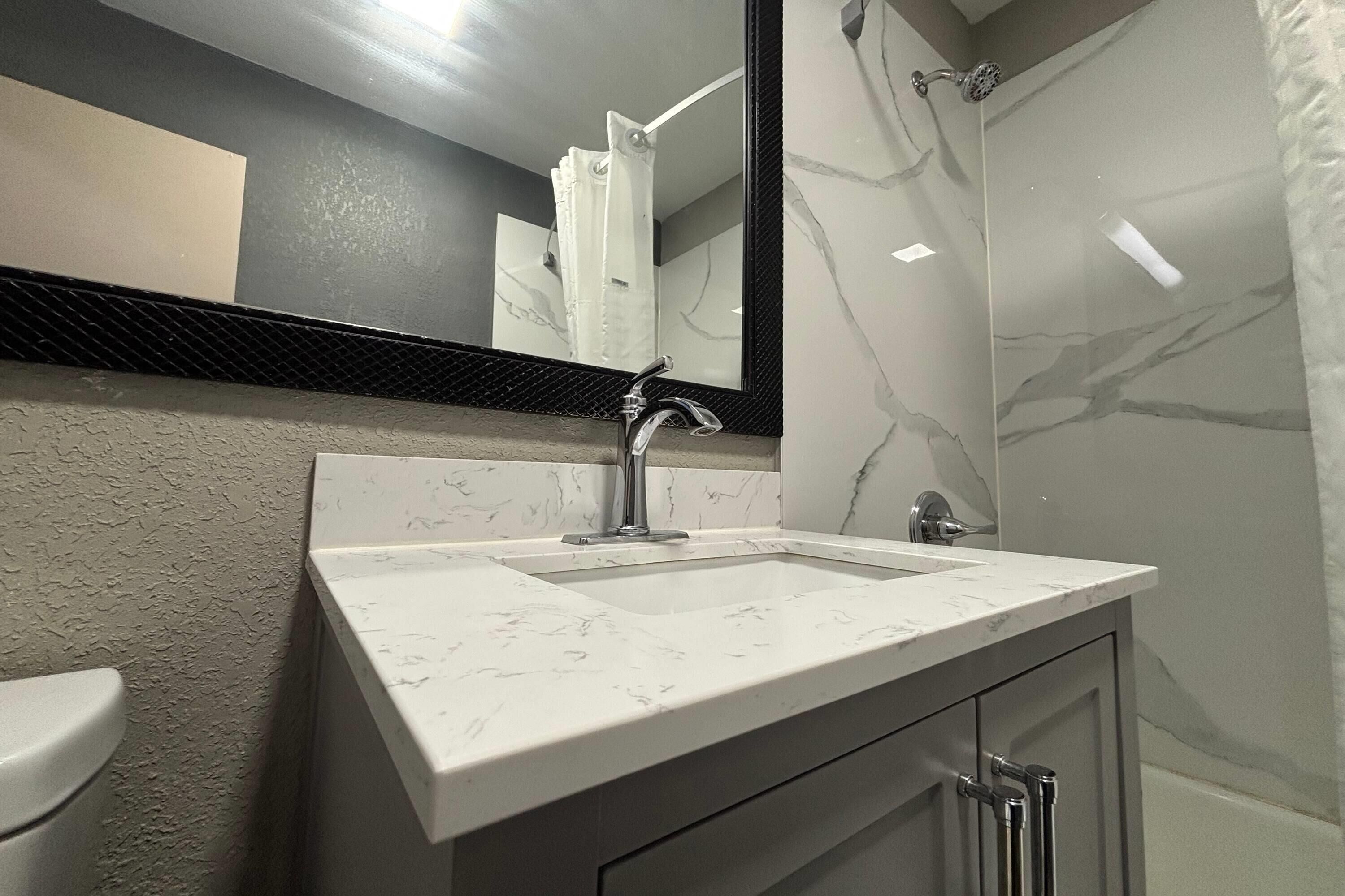 Un baño con lavamanos de mármol, un espejo grande y una ducha.