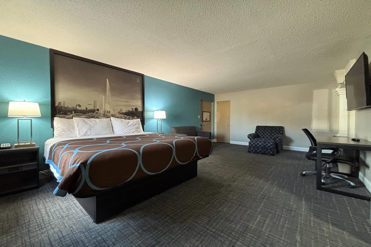 A hotel room with a large bed, two bedside tables with lamps, a desk with a chair, and a television on the wall.