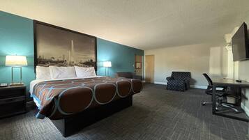 Habitación de hotel con una cama grande, dos mesitas de noche con lámparas, un escritorio con silla y un televisor en la pared.
