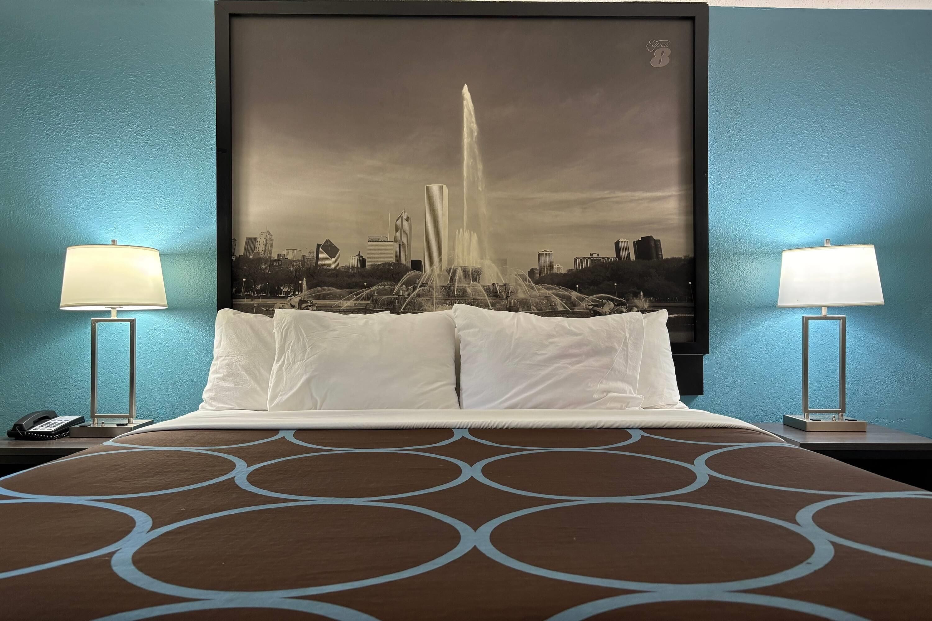 Habitación de hotel con una cama grande, dos lámparas de noche, un cuadro de paisaje urbano en la pared y una colcha estampada.