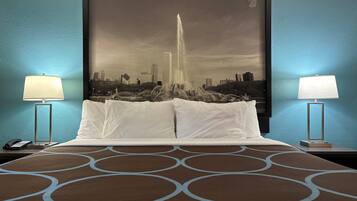 A hotel room with a large bed, two bedside lamps, a cityscape painting on the wall, and a patterned bedspread.