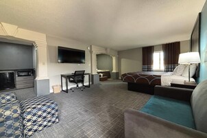 A hotel room with a bed, a desk with a chair, a TV mounted on the wall, and a sofa.