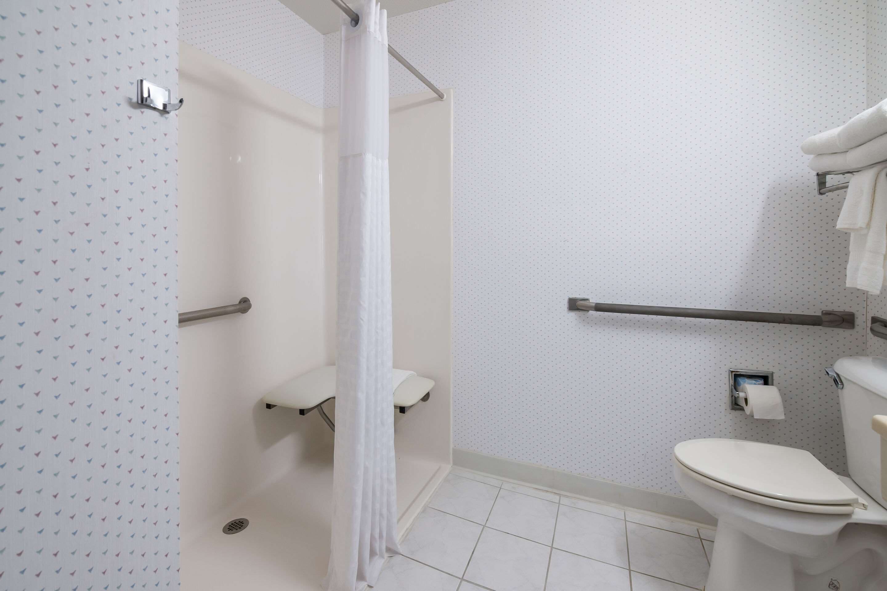 Un baño con ducha, inodoro y barras de apoyo.