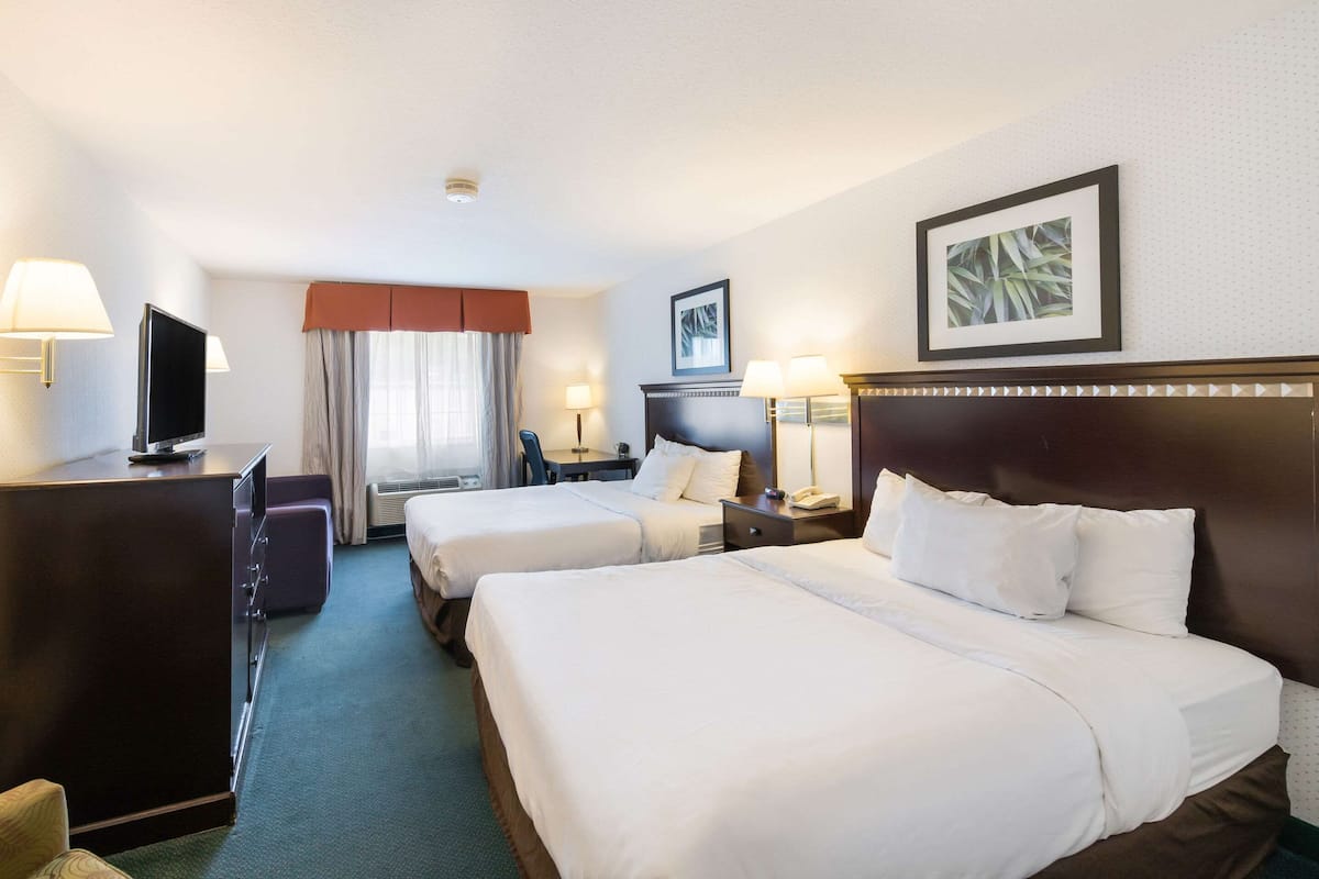 A hotel room with two beds, a desk, a television, and a window with curtains.