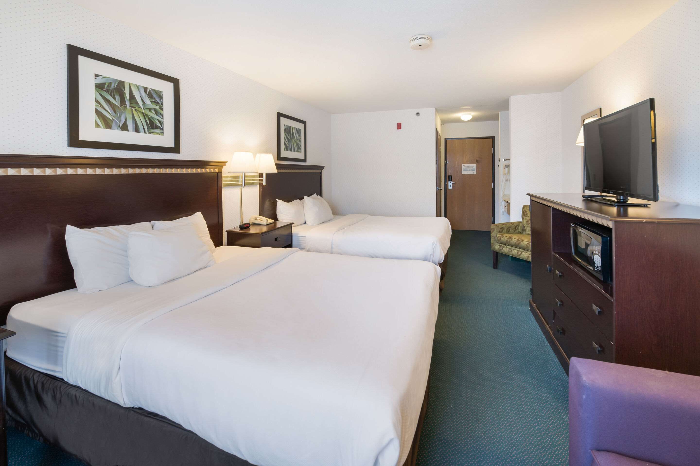 Una habitación de hotel con dos camas, un televisor, un aparador y una puerta que da a otra habitación.