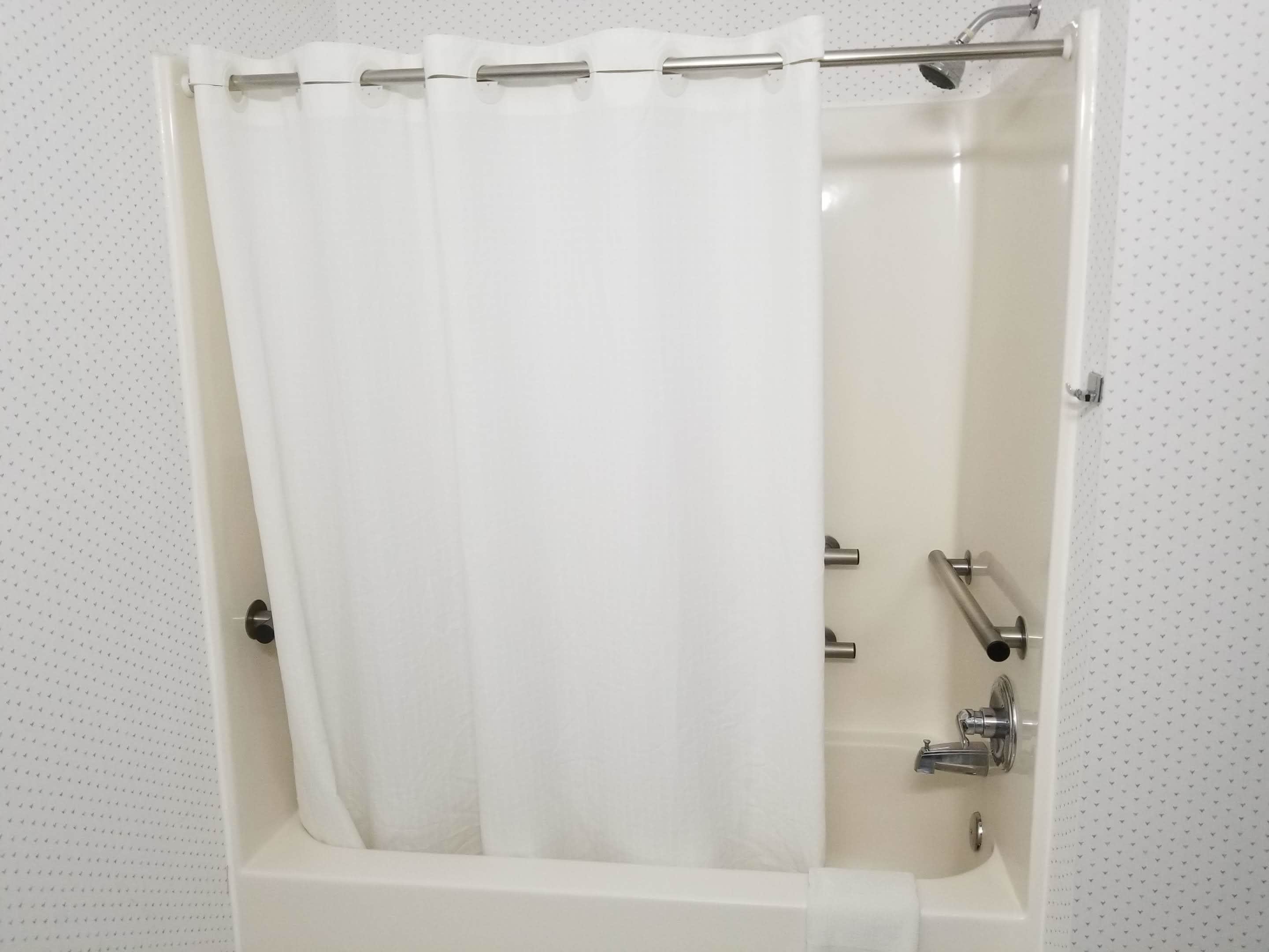 Una bañera estándar con cortina de ducha, cabezal de ducha de mano y grifo.