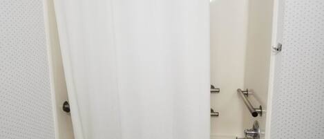 Una bañera estándar con cortina de ducha, cabezal de ducha de mano y grifo.