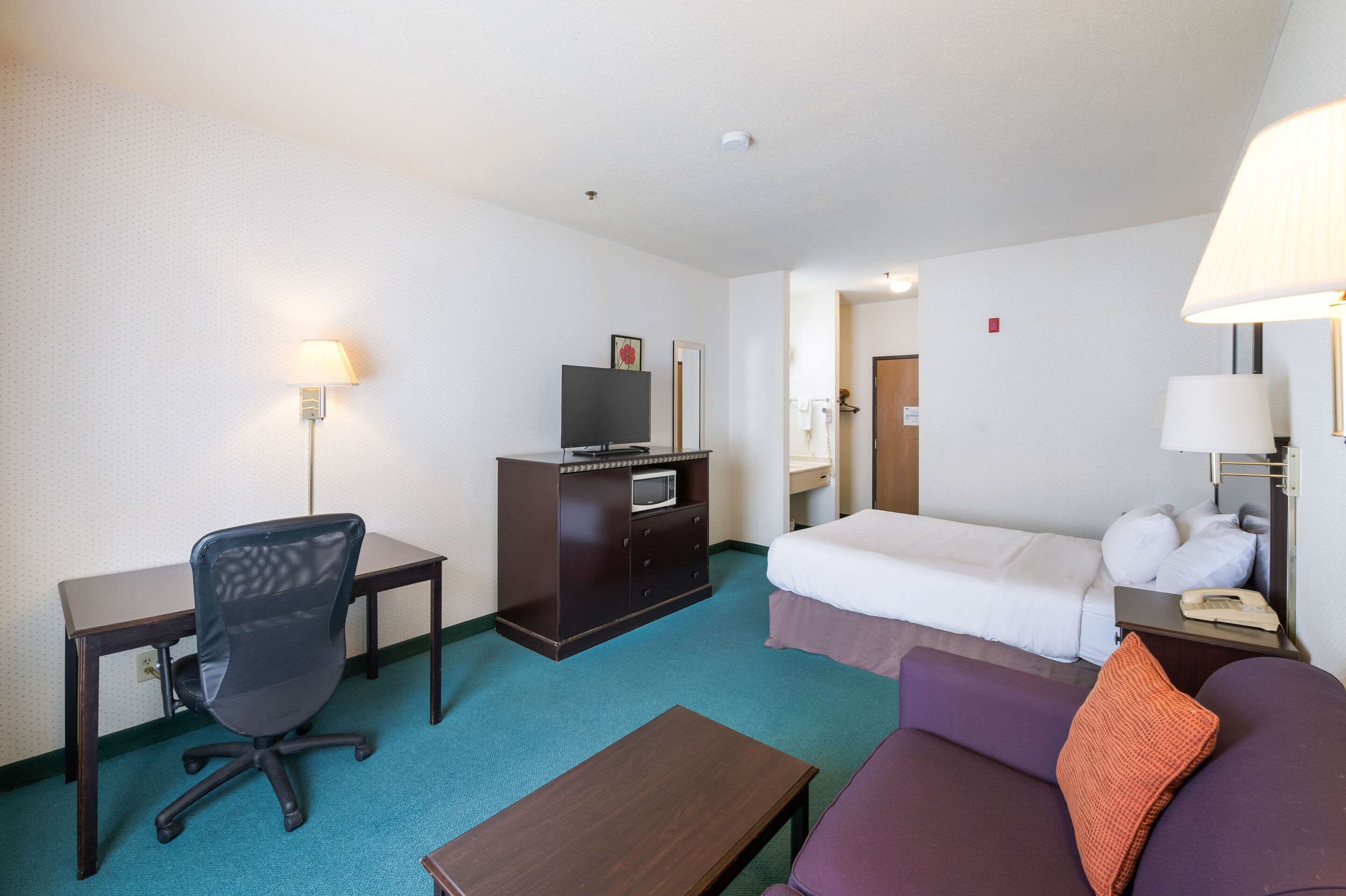 Habitación de hotel con cama, escritorio, silla, mesita, televisor y lámpara.