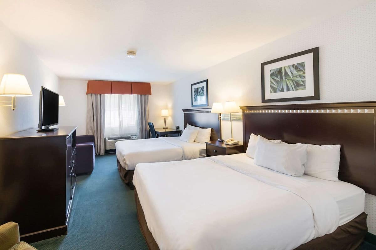 A hotel room with two beds, a desk, a TV, and a window with curtains.