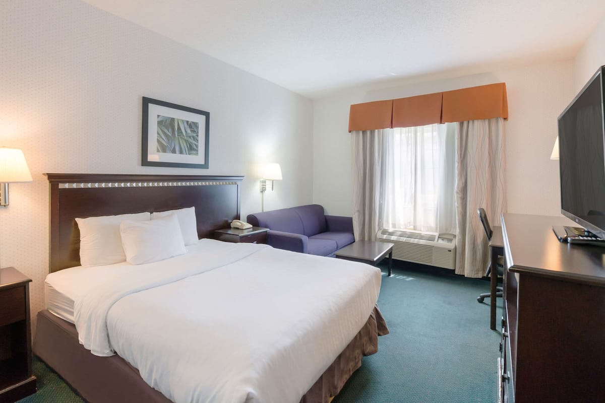 A hotel room with a large bed, a desk, a chair, a television, and a window with curtains.