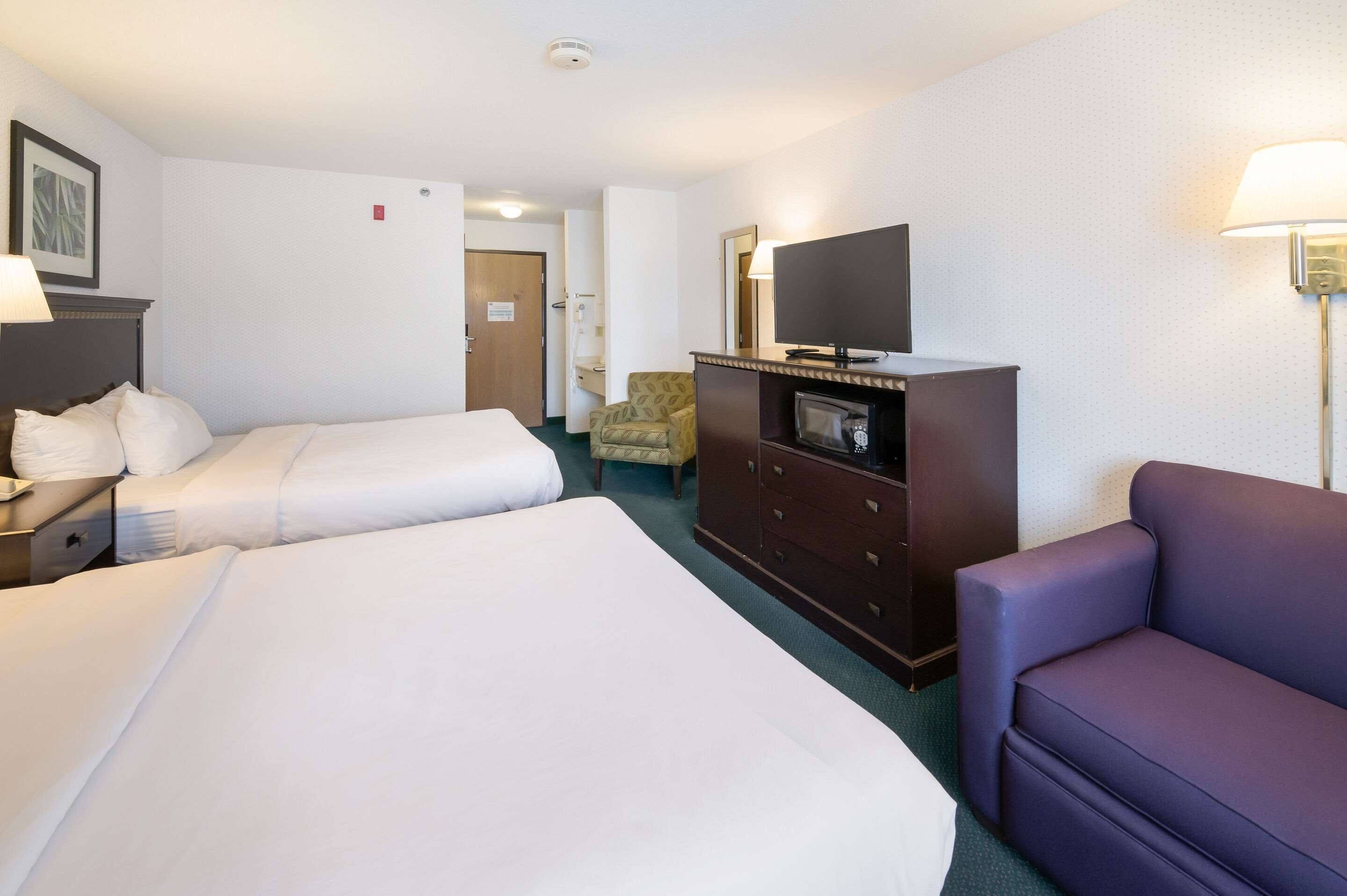 A hotel room with two beds, a TV, a dresser, a chair, and a sofa.