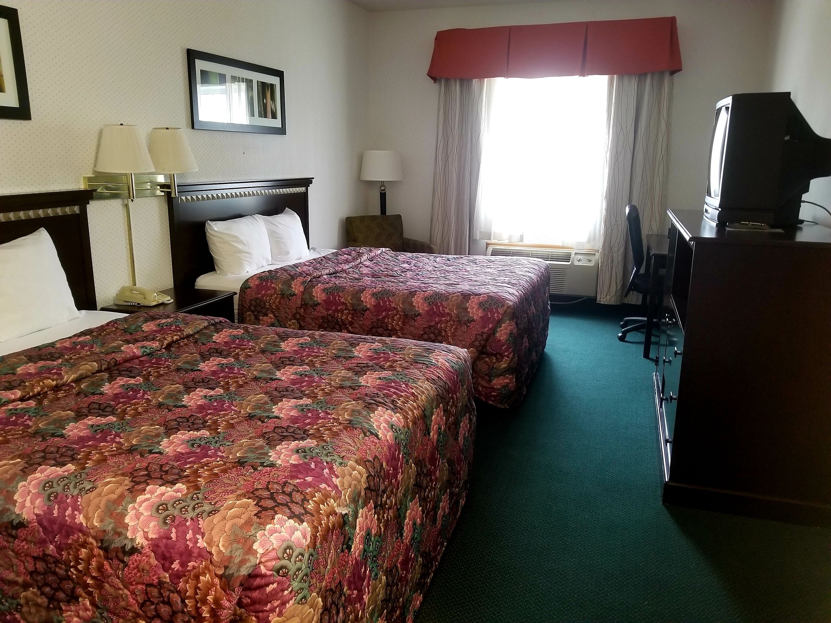 A hotel room with two beds, a desk, a television, and a window with curtains.
