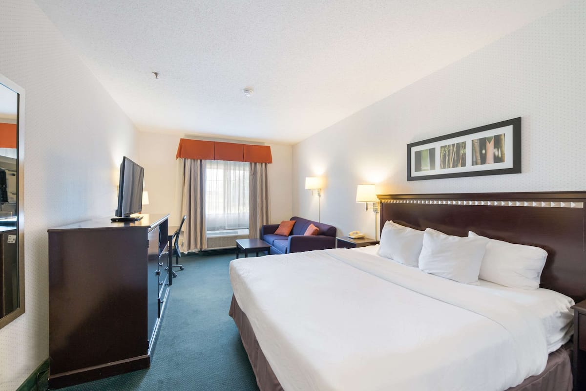 A hotel room with a large bed, a desk with a computer, a TV, and a window with curtains.